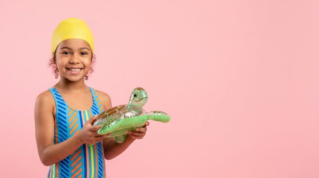 Joyful young girl in swimsuit and swim cap holding a turtle float on pink background with copy space