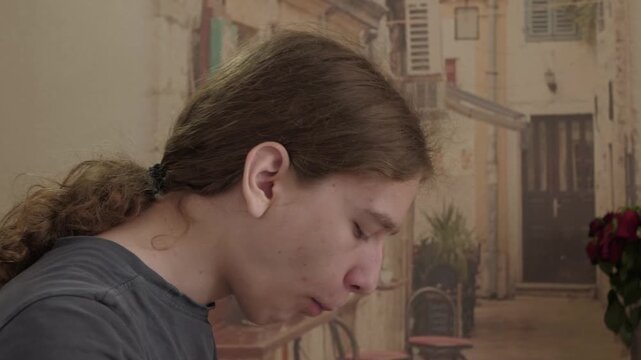 Teenage boy shown in profile eating small snack, chewing softly, relaxed posture, warm indoor light, relaxed posture, and calm everyday mood, with teenager, boy, eating, snack detail
