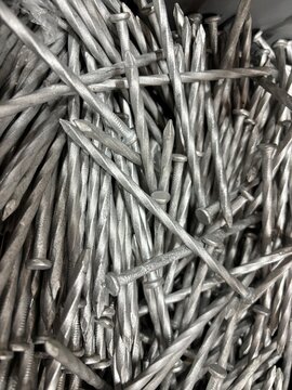 A close-up view of a chaotic pile of silver metal nails, showcasing their sharp points and flat heads in a monochromatic industrial texture