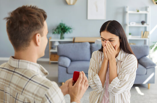 Marry me, young man holding red box with marriage engagement ring, preparation make proposal to loving surprised woman, girlfriend covering face in hands, lover offering romantic Valentine's day gift