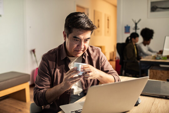 Man drinking coffee while working on laptop in modern office