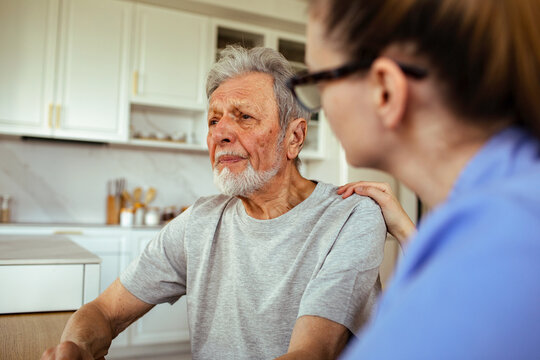 Caregiver comforting senior man in kitchen at home