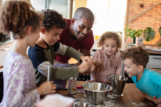Smiling father baking with children in home kitchen