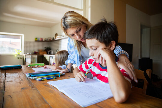 Mother helping son with homework at kitchen table at home