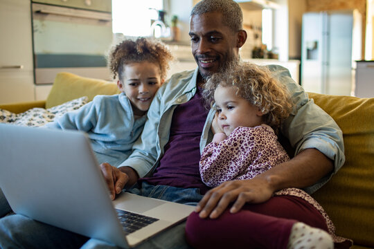 Father with two children using laptop on sofa at home