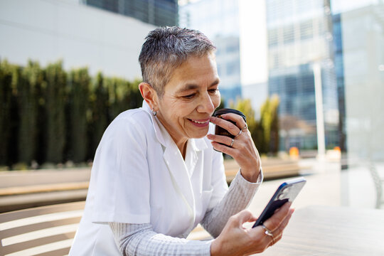 Smiling senior woman using smartphone with coffee outdoors in city