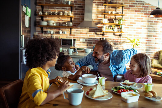 Smiling dad and kids eating breakfast in home kitchen