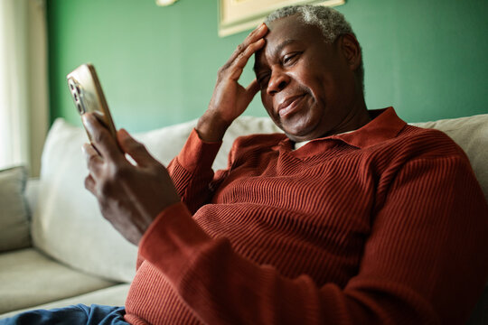 Concerned senior man reading smartphone at home on sofa