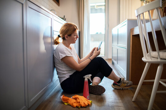 Woman taking a cleaning break in a home kitchen while checking smartphone