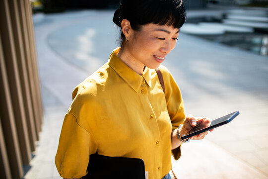 Smiling businesswoman using smartphone outdoors in city