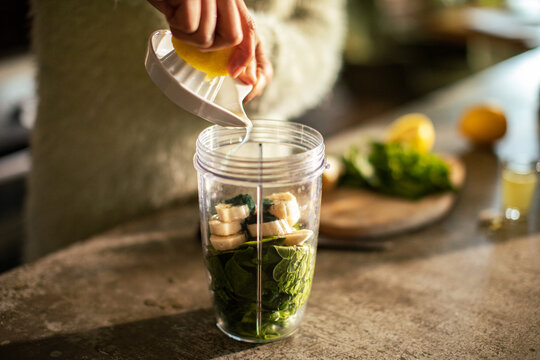 Person squeezing lemon into smoothie blender cup in home kitchen
