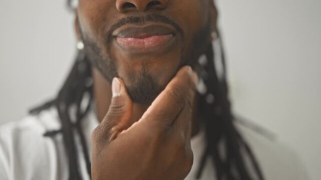 Young african american man stroking chin and beard with hand in a studio closeup; thoughtful introspection.