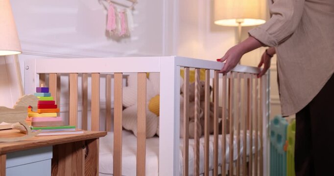 Woman putting toy bear into crib in baby's room, closeup
