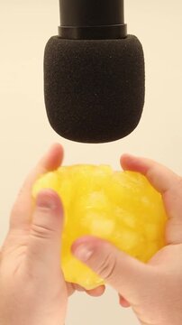 Two hands slowly knead and form soft yellow goo into a round ball next to a microphone, squeezing, bending and stretching the sticky texture in close-up ASMR footage.