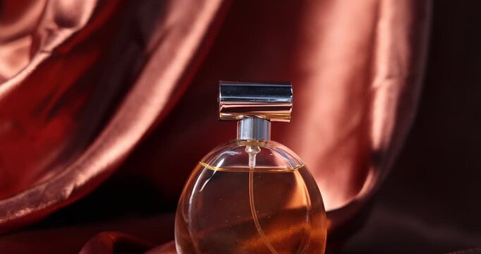 Bottle of aromatic perfume on brown silk, closeup. Camera moving backwards