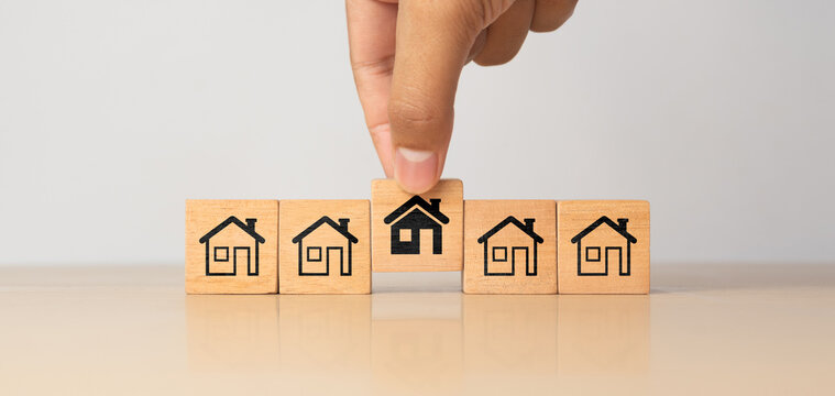 Real estate management, Property, Asset investment concept. Hand picking wooden cube block with house icon from others. Family makes the best decision when choosing the housing you truly want