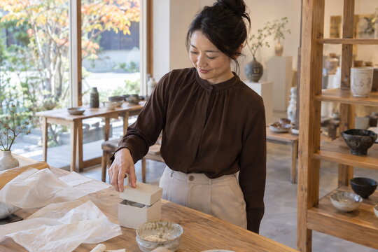 陶器店の木製テーブルで贈り物の小箱の蓋を扱う日本人女性