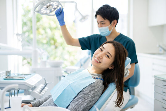 診察前にライトを調整する歯科医師と笑顔の女性患者のいる歯科医院