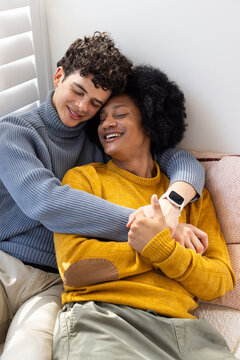 African American male partners sitting on light sofa near window shutters, wearing knit sweaters