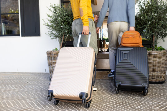 Two African American men pulling beige and black rolling suitcases on herringbone tile porch