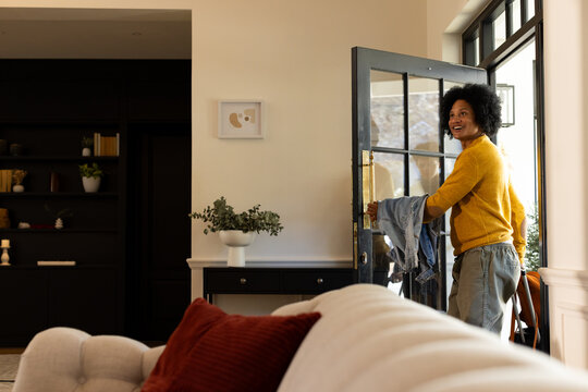 African American woman standing at front door holding denim jacket looking back inside, copy space