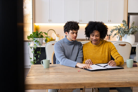 African American male family studying black binder at kitchen table in gray and mustard sweaters