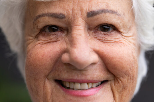 Senior female smiling and showing eyebrow makeup, pink lipstick, teeth in close-up studio portrait