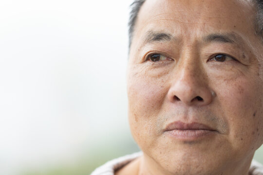 Senior Chinese man gazing left near window, showing light collar and fine wrinkles, copy space