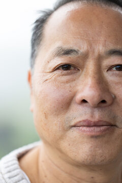 Senior Chinese man gazing at camera, showing wrinkles and stubble, wearing knitted sweater outdoors