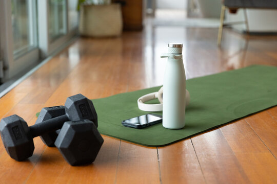 White water bottle standing on green yoga mat near sliding doors, phone and headphones nearby