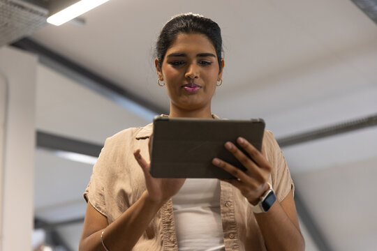 Indian woman wearing beige overshirt standing in office holding tablet in folio with smartwatch
