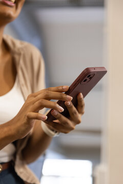 Indian woman in 20s holding maroon phone tapping screen in lobby wearing beige shirt white watch