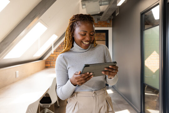 Mid-adult African American woman standing in loft office holding tablet, smiling under skylights