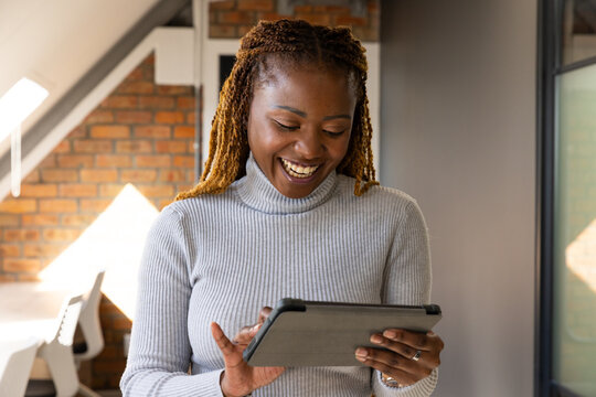 African woman standing in modern workspace smiling and looking at tablet in folio case