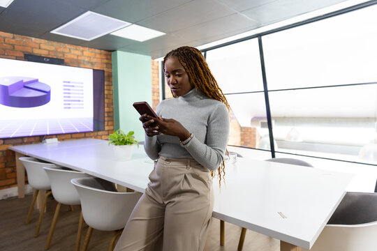 Woman leaning on table in office checking phone with screen in turtleneck, copy space