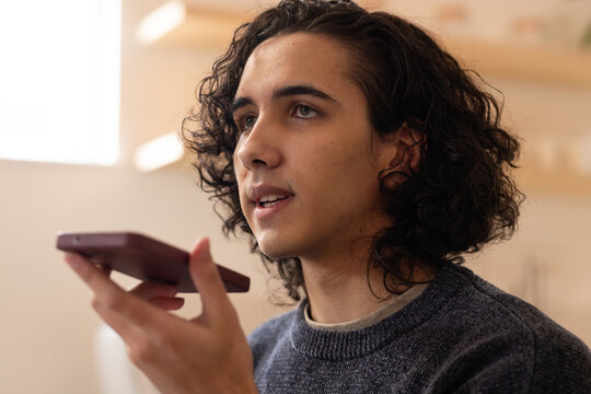 African American man wearing gray sweater holding smartphone to mouth speaking into device at home