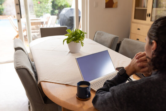 Male working at dining table using silver laptop and mug in dark sweater, copy space