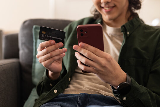 African American man holding red phone and dark card on sofa wearing dark green shirt, smartwatch