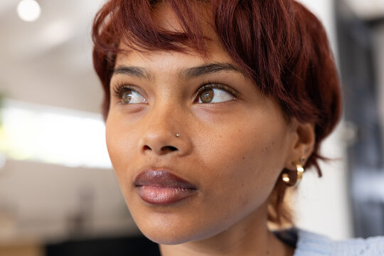African American woman gazing upward wearing light blue top, nose stud and gold hoops in studio