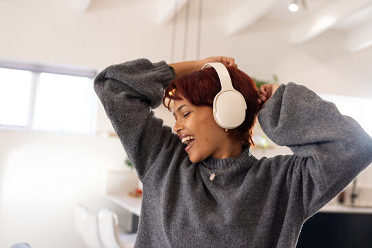 African American woman singing with arms raised in home kitchen wearing white headphones