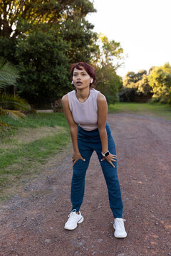 African American woman pausing with hands on knees on dirt path in sportswear with smartwatch