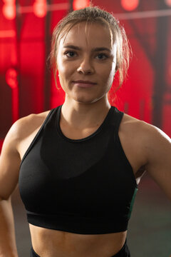 Female in 20s standing facing camera in gym with black sports bra, rigs and red backlights