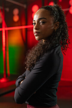 Adult woman posing arms crossed in studio wearing black longsleeve top maroon pants with light bars