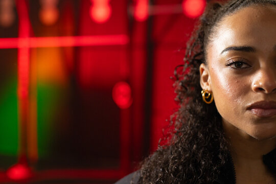 African American woman wearing zip jacket and gold hoops gazing onstage with LED lights, copy space