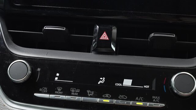 Video of a woman's hand pressing the hazard warning triangle button on a car dashboard, activating the emergency lights