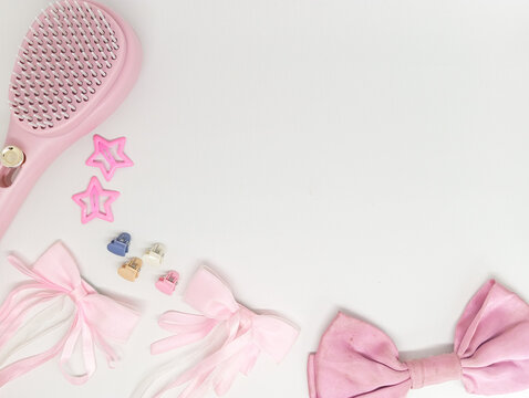 Creative border composition of pink hairbrush, ribbons, and star hair clips isolated on white background.