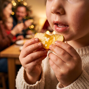 close-up photography of a child's hands carefully holding a small slice of apple covered in glistening honey, about to take a bite. The warm golden light highlights the child's face and the sticky tex