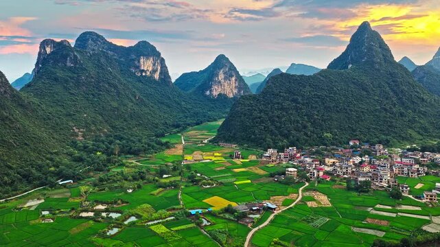 Aerial view of karst mountains and rural village with rice paddies at sunset in Guilin, China.