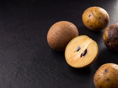 Fresh buah kepel whole and halved showing yellow flesh with seeds on dark background