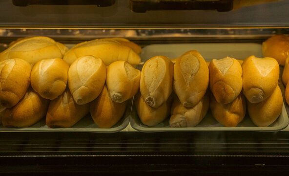 Freshly baked bread rolls, cut lengthwise, sit in plastic trays behind a glass display case.
